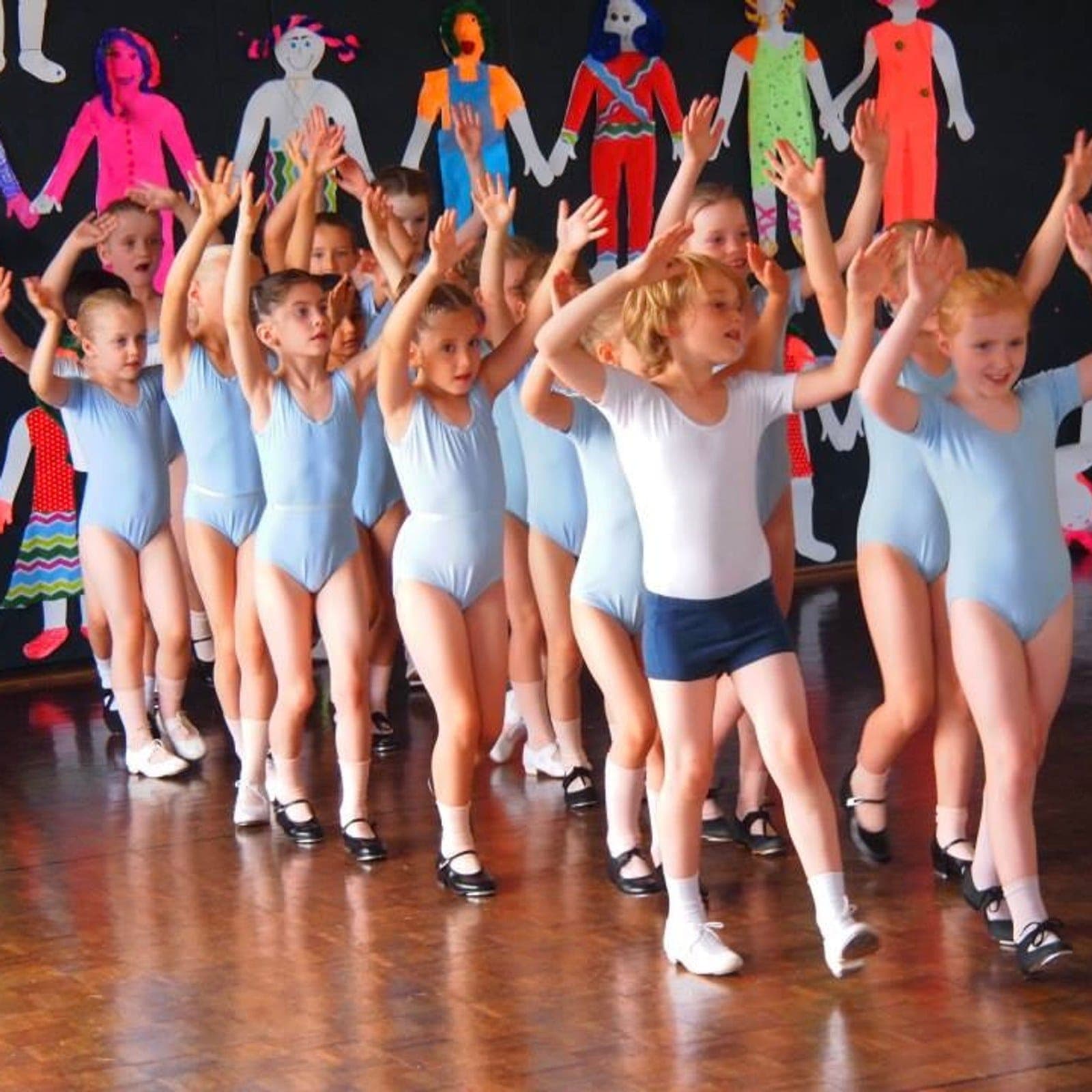 Junior dancers in light blue leotards with arms raised on stage