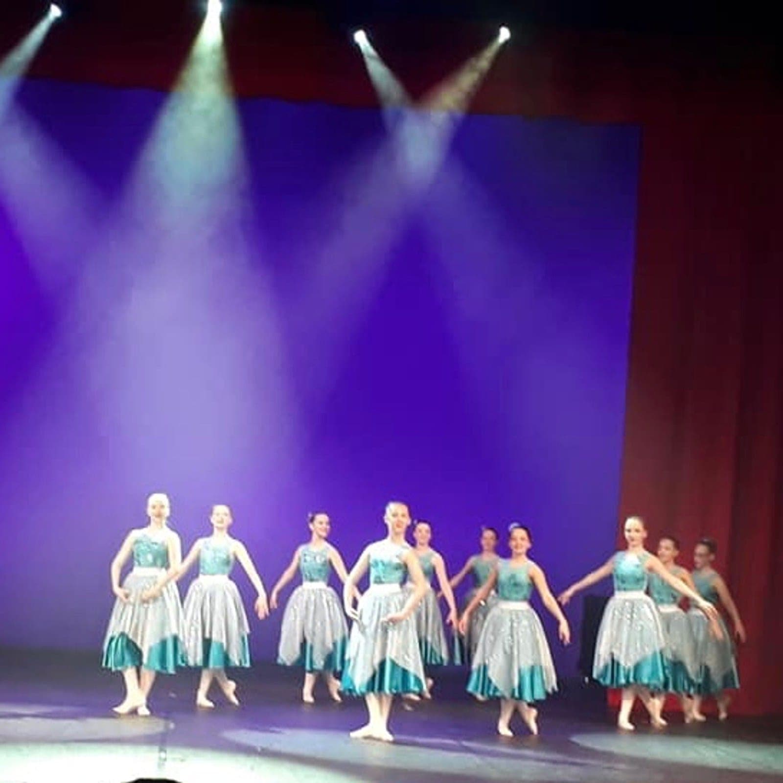 Line of dancers in teal and silver costumes under spotlights